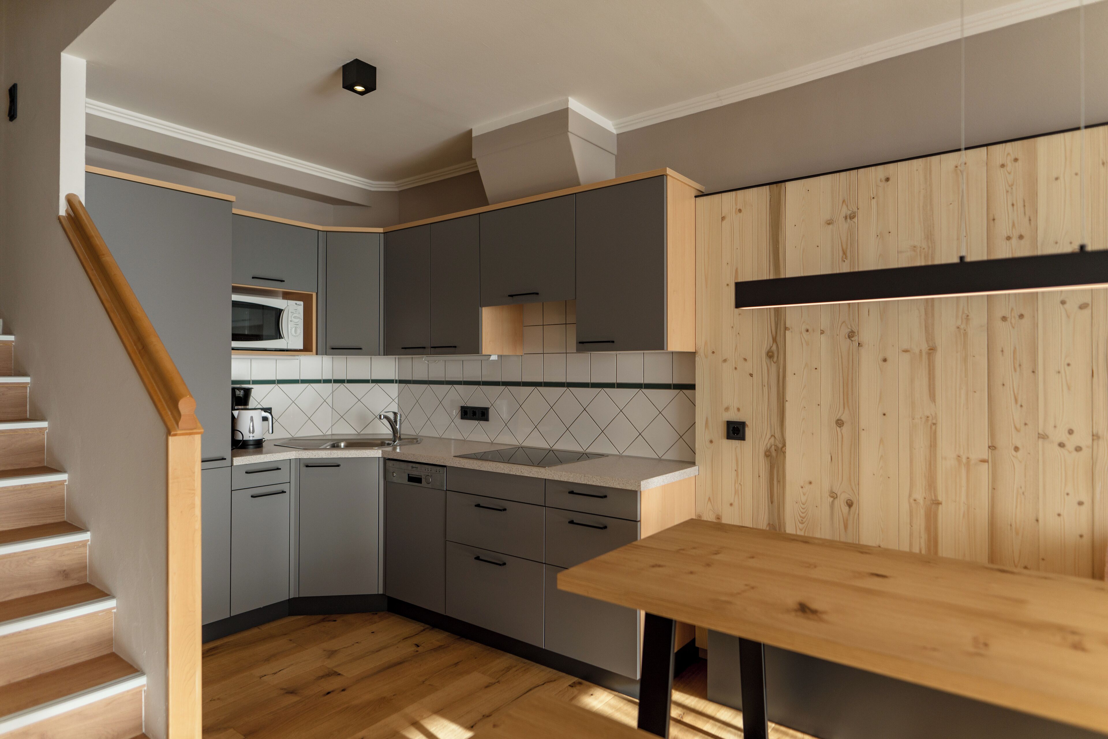 Una cocina moderna con armarios grises, una mesa de madera y un salpicadero de azulejos.