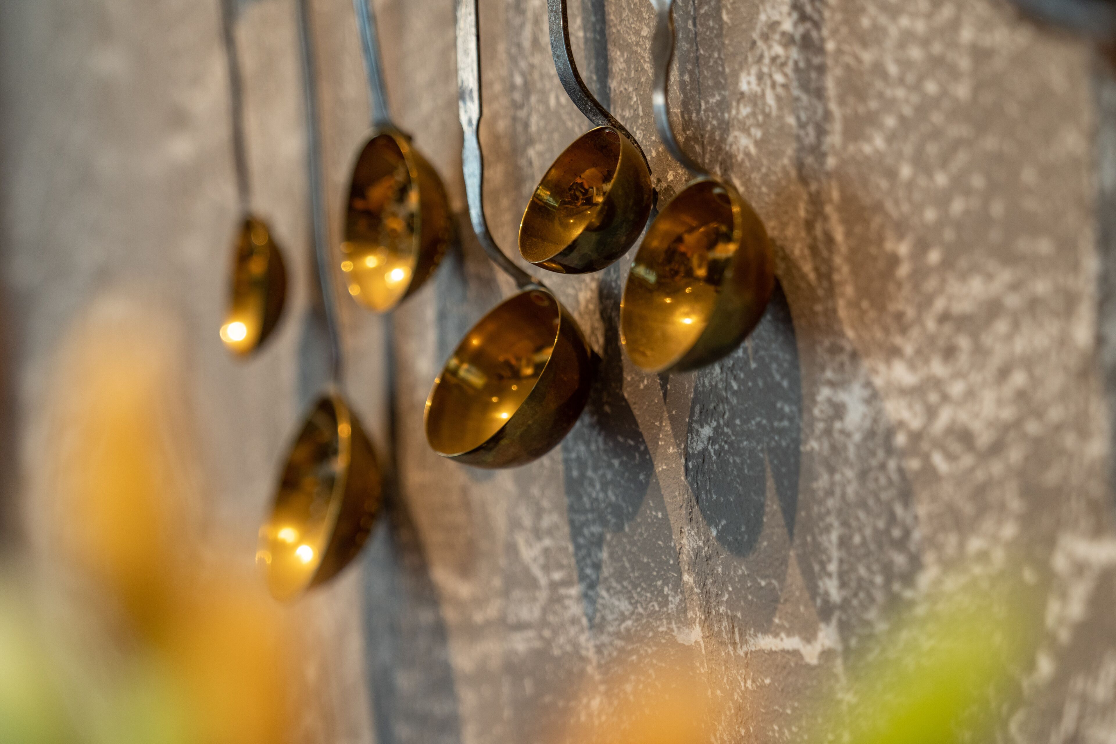 A close-up of a textured wall with a series of metallic spoons hanging from it.
