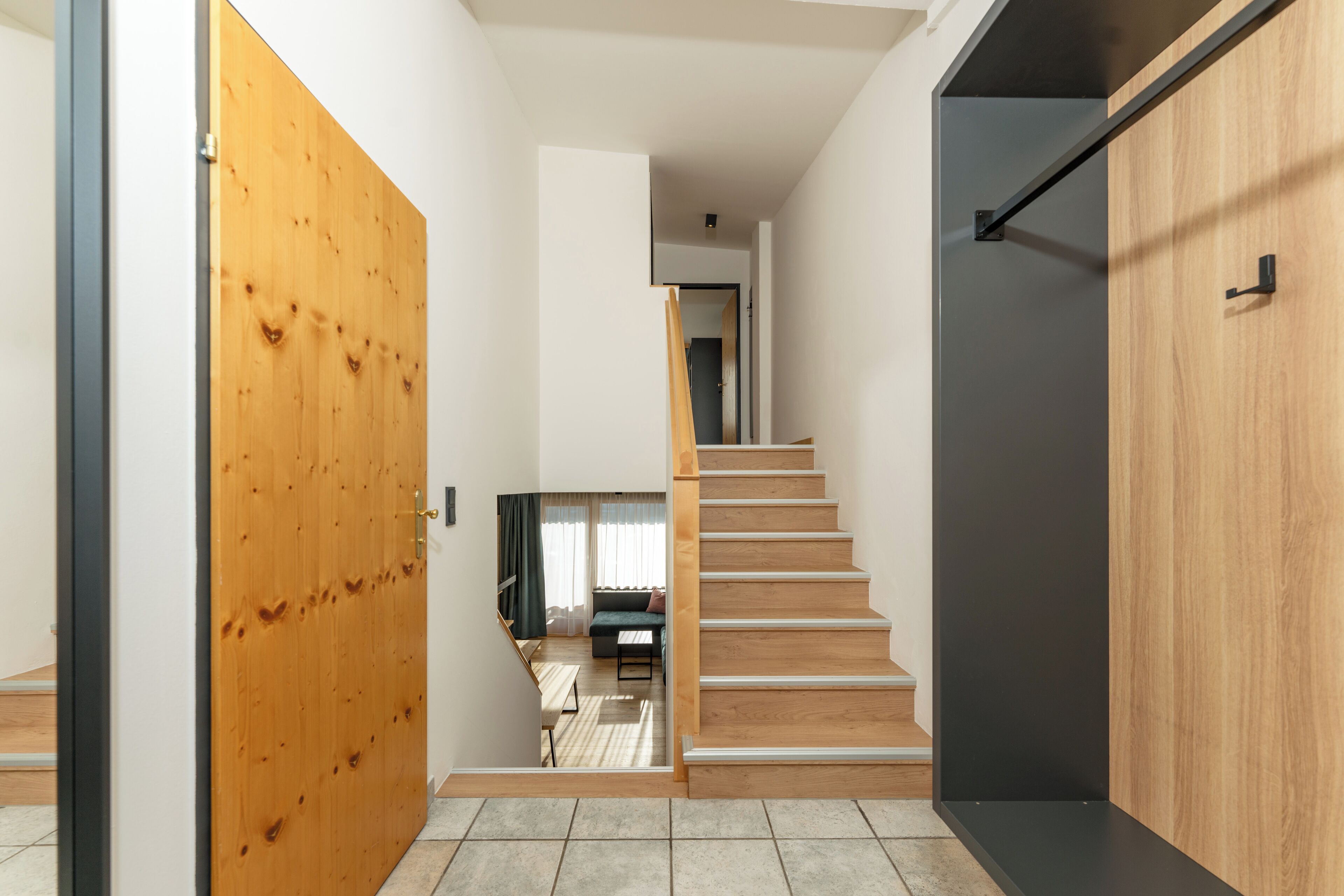 Een modern interieur met een houten deur, een trap en uitzicht op een zithoek met een bank en salontafel.