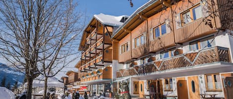 A wooden multi-story building with balconies, a snow-covered ground, and a clear sky.