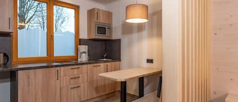 A modern kitchen with wooden cabinets, a built-in microwave, a coffee maker, and a small dining table.