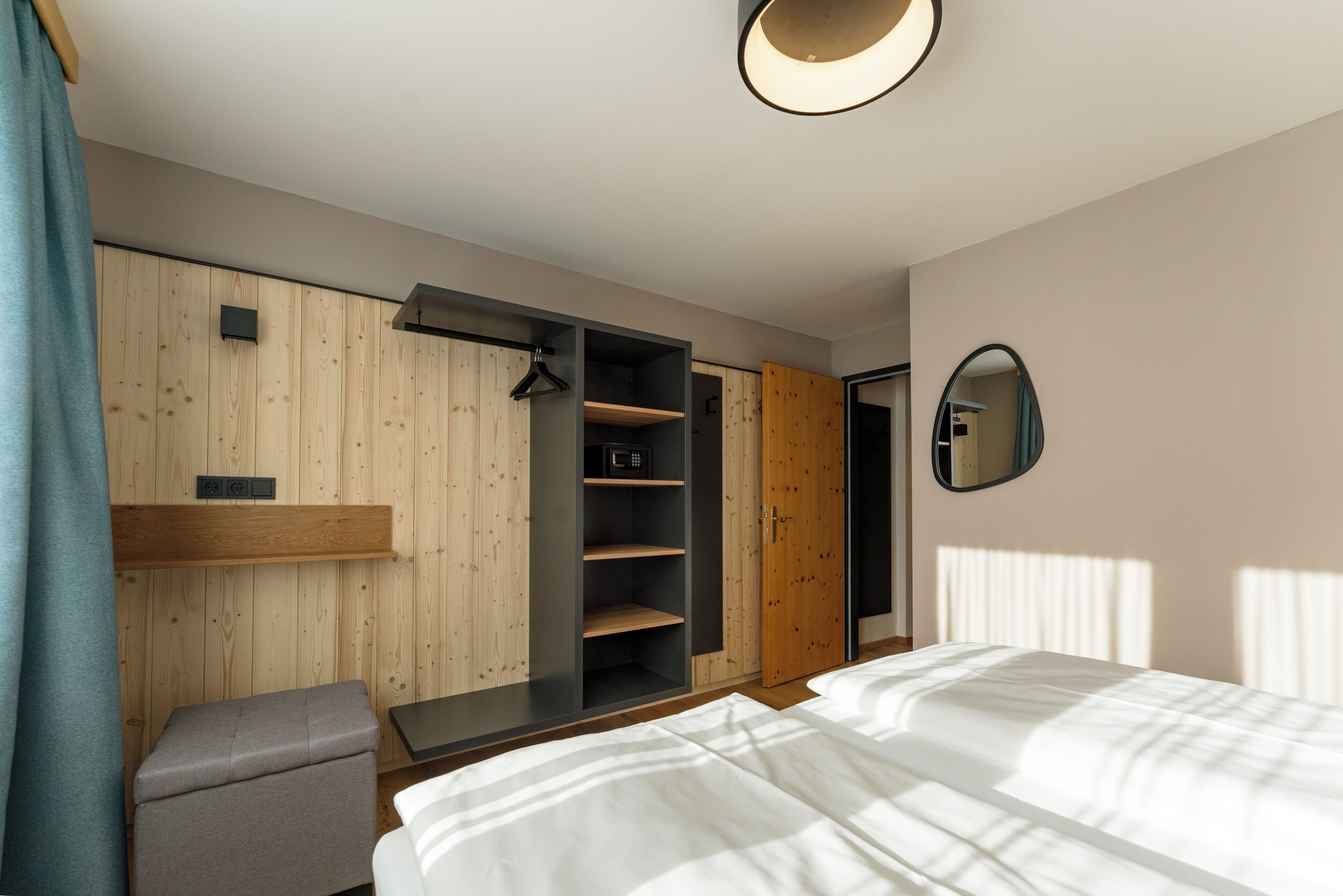 Une chambre moderne avec un lit, une armoire en bois, un petit coin salon et un miroir au mur.
