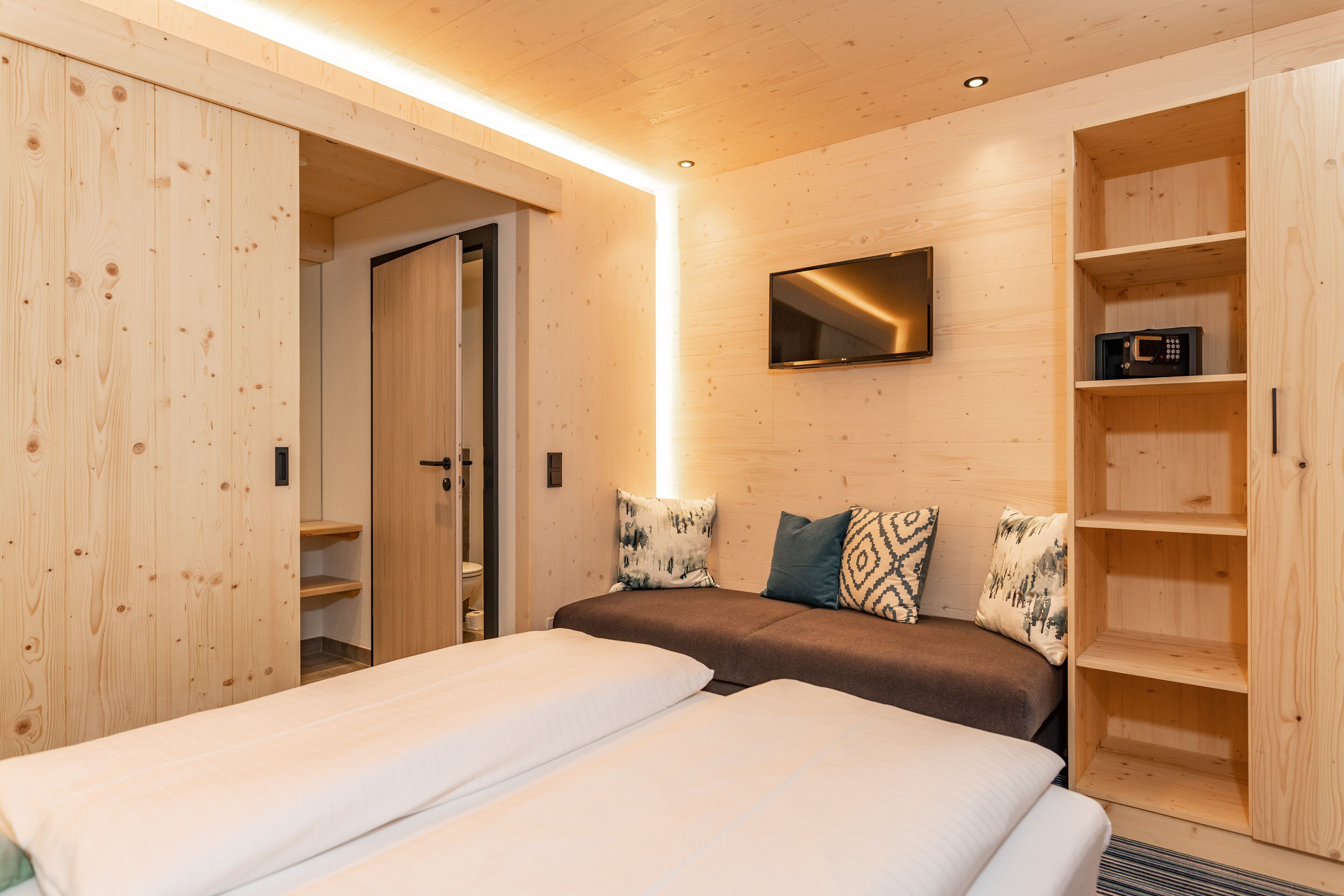 A room with two beds, a TV mounted on the wall, and wooden shelving units.