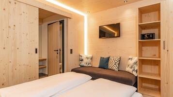 A room with two beds, a TV mounted on the wall, and wooden shelving units.