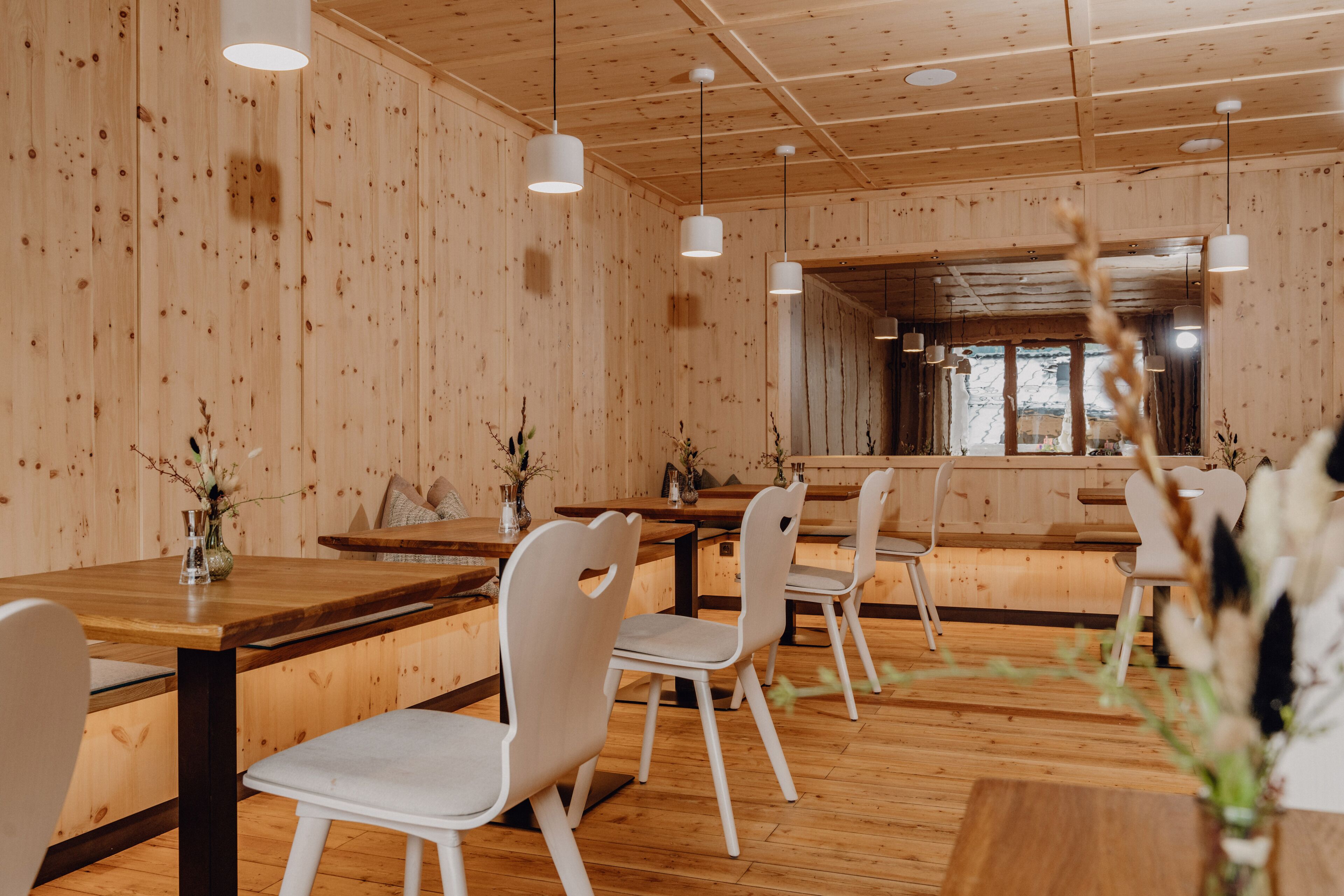 A restaurant with wooden walls and ceiling, white chairs, and hanging pendant lights.
