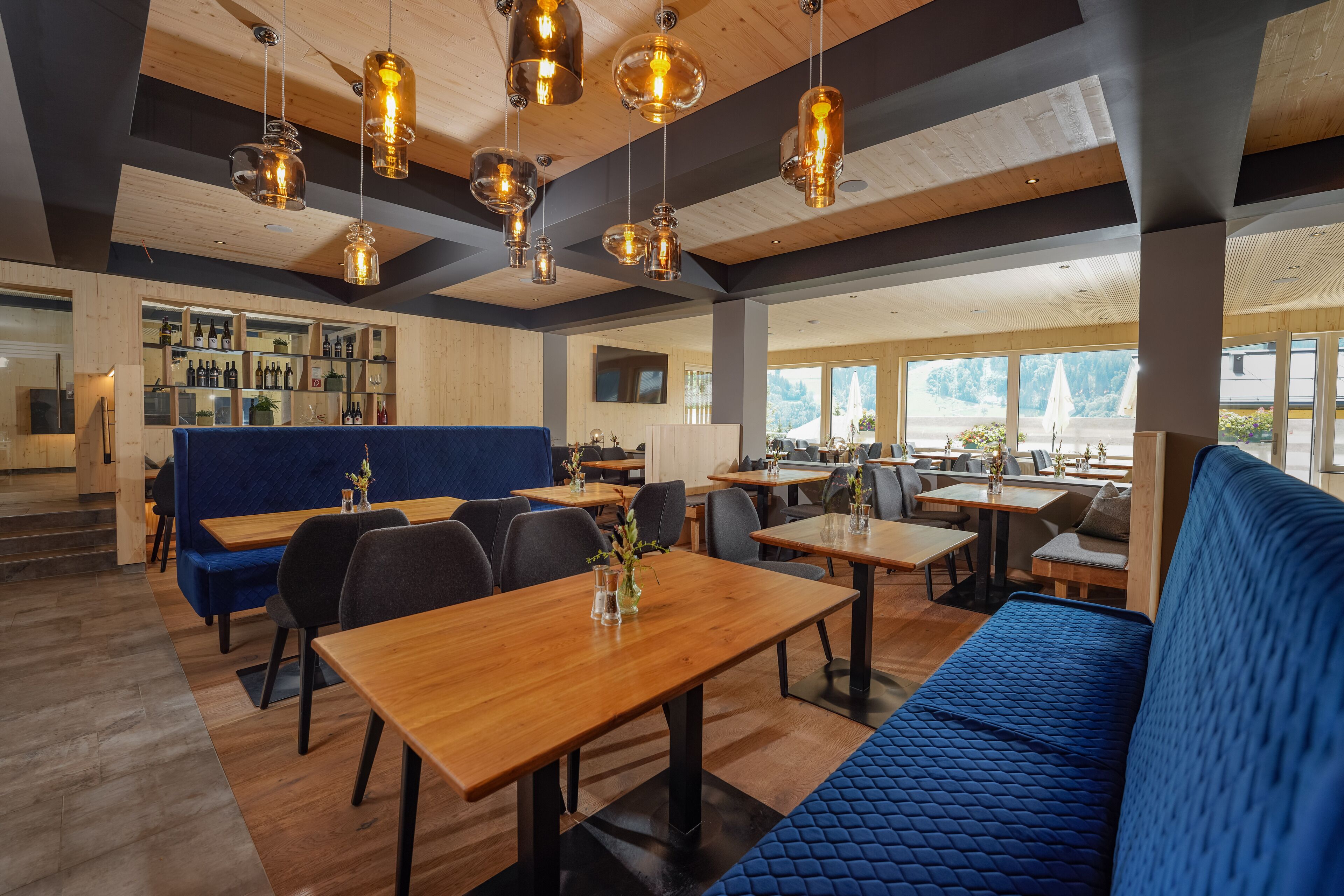 A modern restaurant interior with wooden tables, blue seating, and hanging pendant lights.