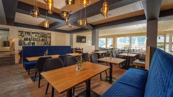 A modern restaurant interior with wooden tables, blue seating, and hanging pendant lights.