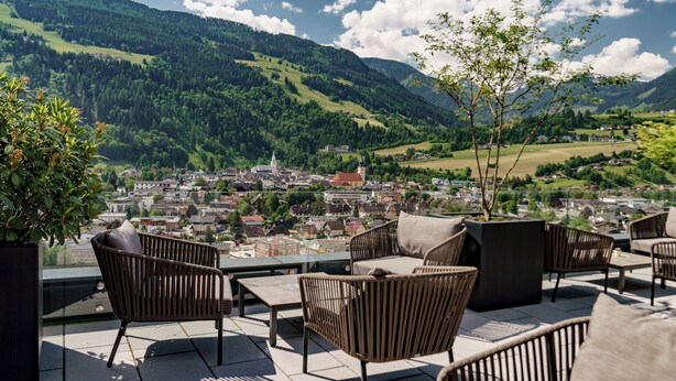 A terrace with wicker furniture and a view of a town and mountains. - Ferienalm Panorama Hotel & Apartments (Schladming)