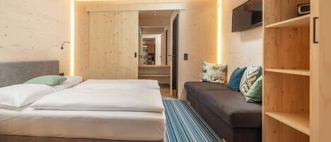 A modern hotel room with a large bed, a sofa, and a wooden wardrobe.
