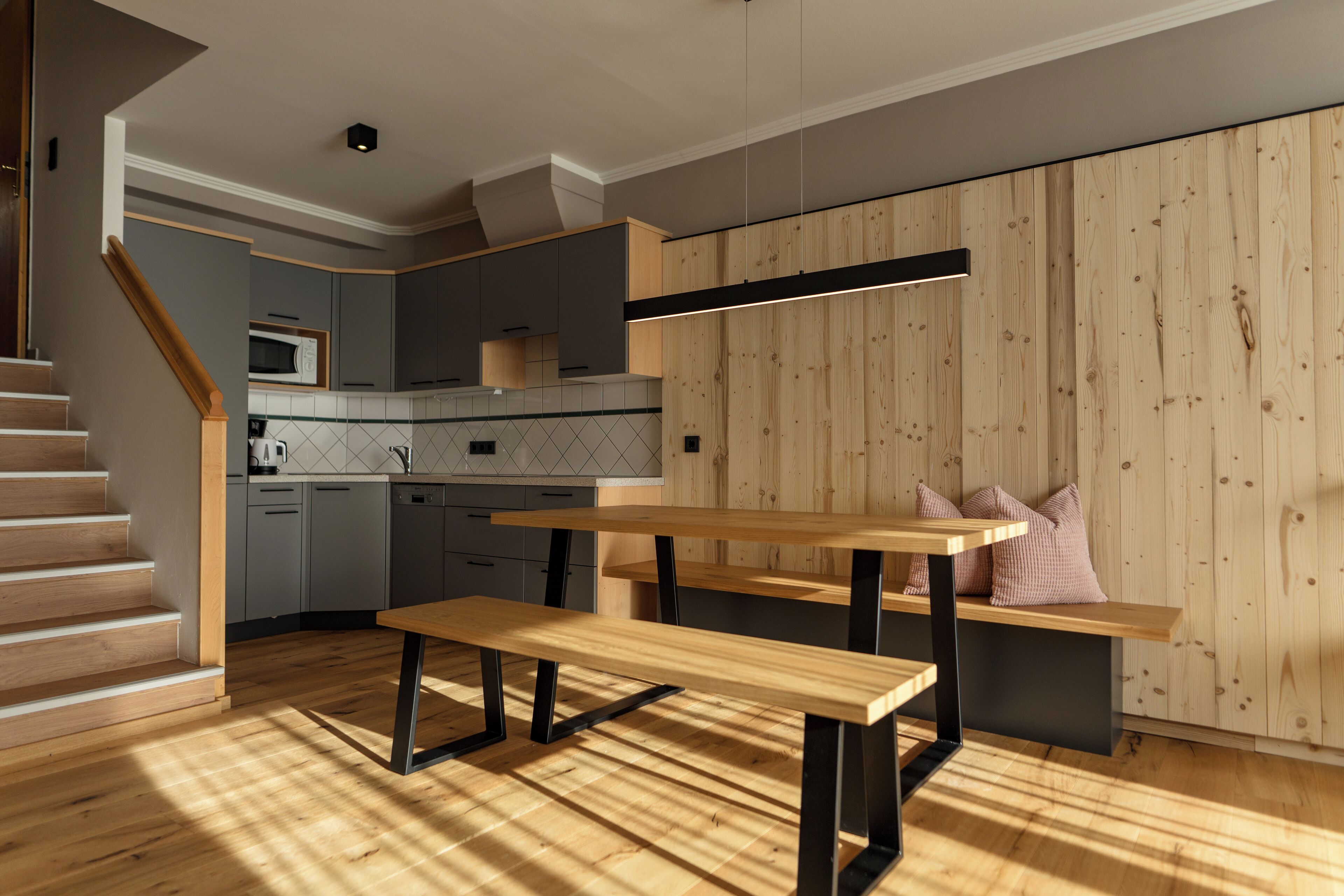 A modern kitchen with wooden flooring, built-in appliances, and a dining area with a bench and table.