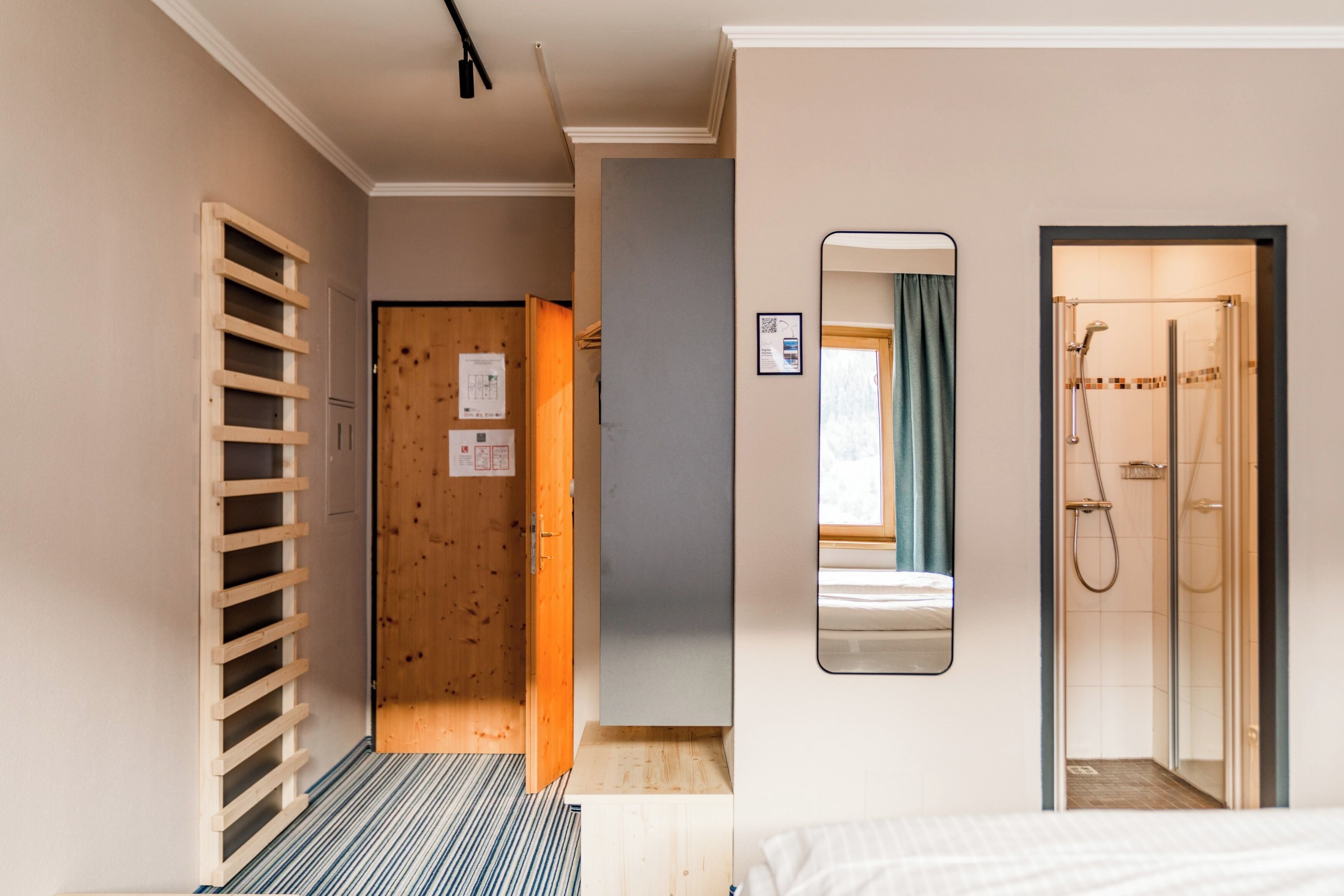 A hotel room with a bed, a wooden ladder, a shower, and a mirror on the wall.