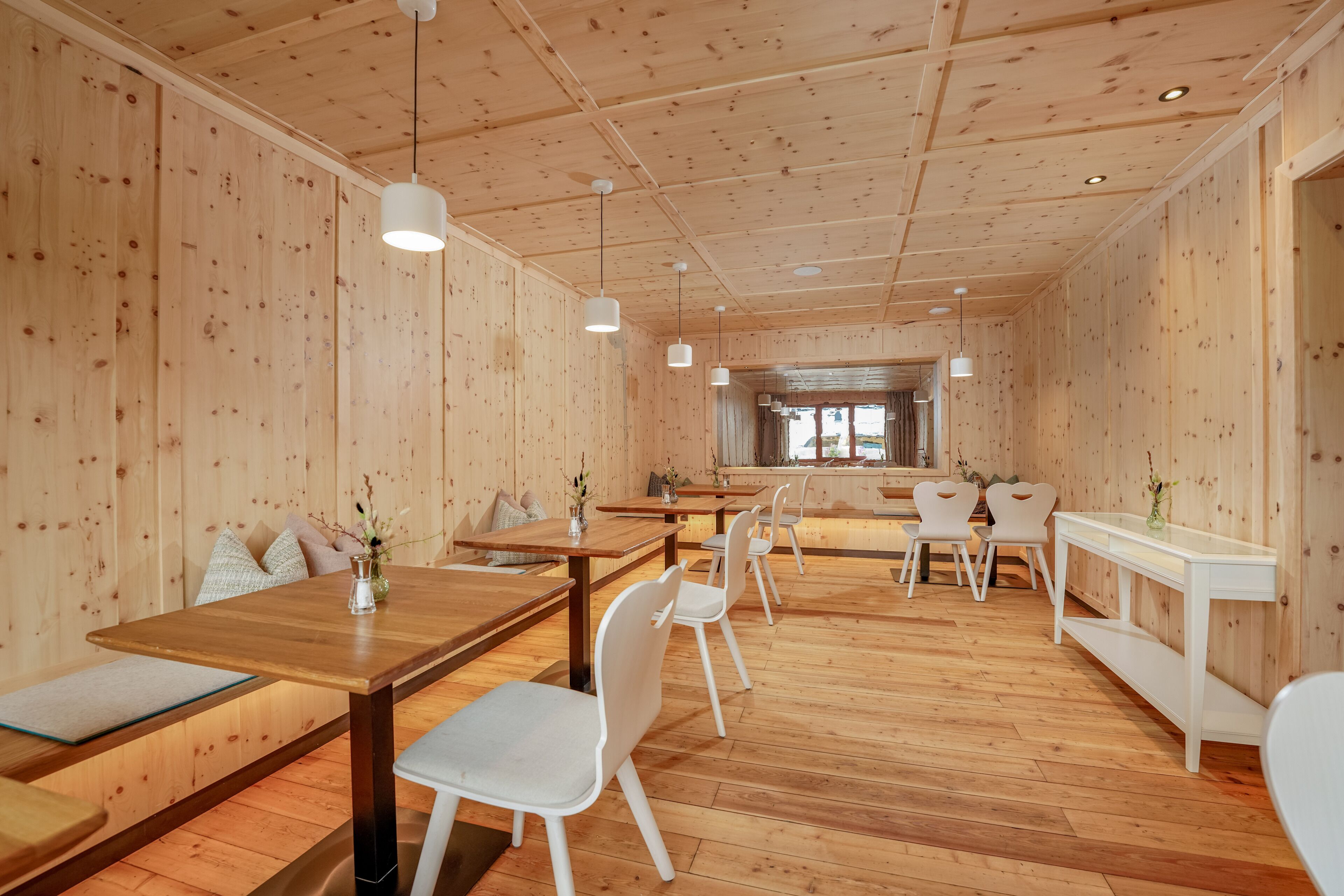 Een houten interieur met tafels, stoelen, een bank en hangende lampen.