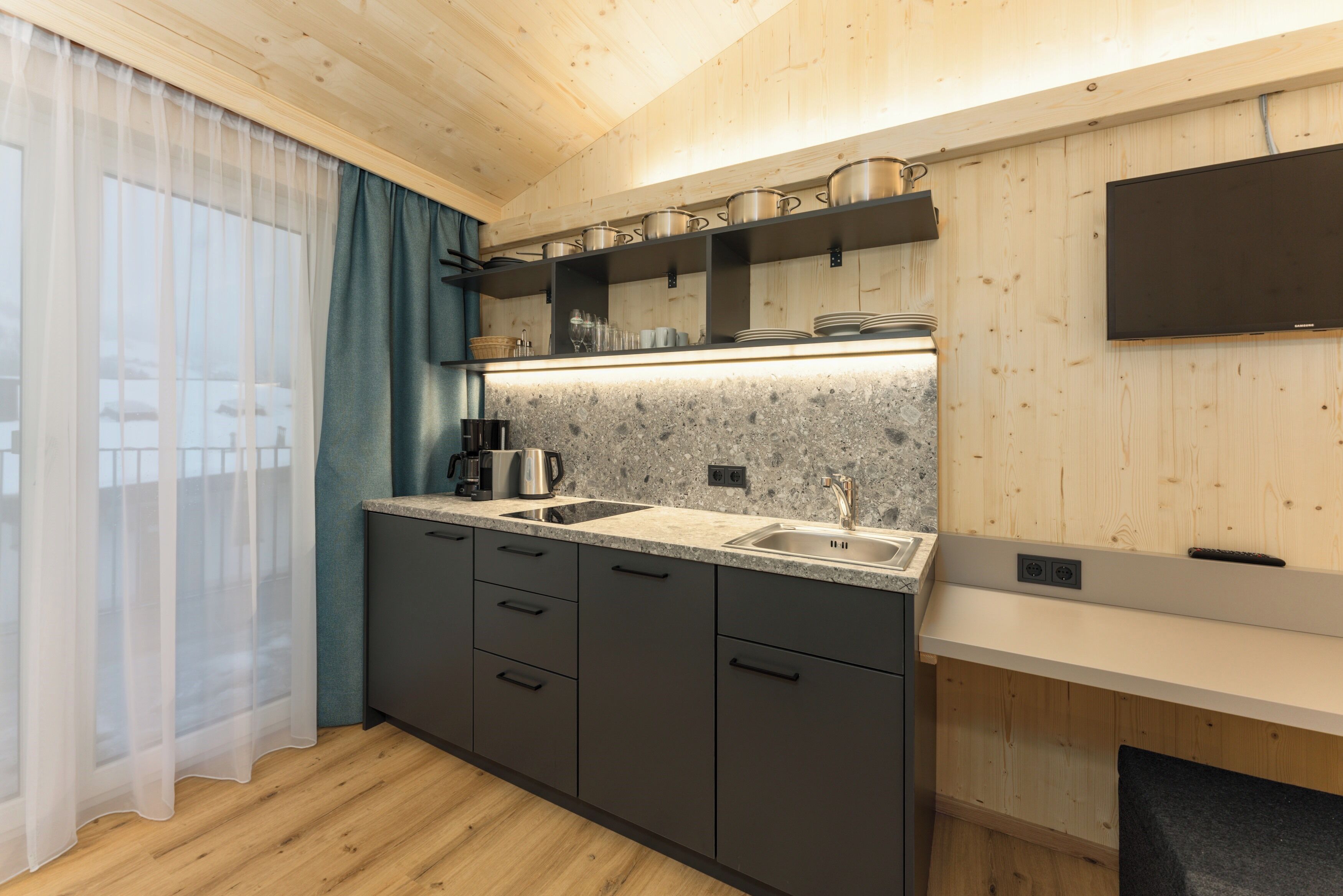 Une cuisine moderne dotée de plans de travail en granit, de meubles de rangement sombres, d’un évier en acier inoxydable et d’un four encastré.