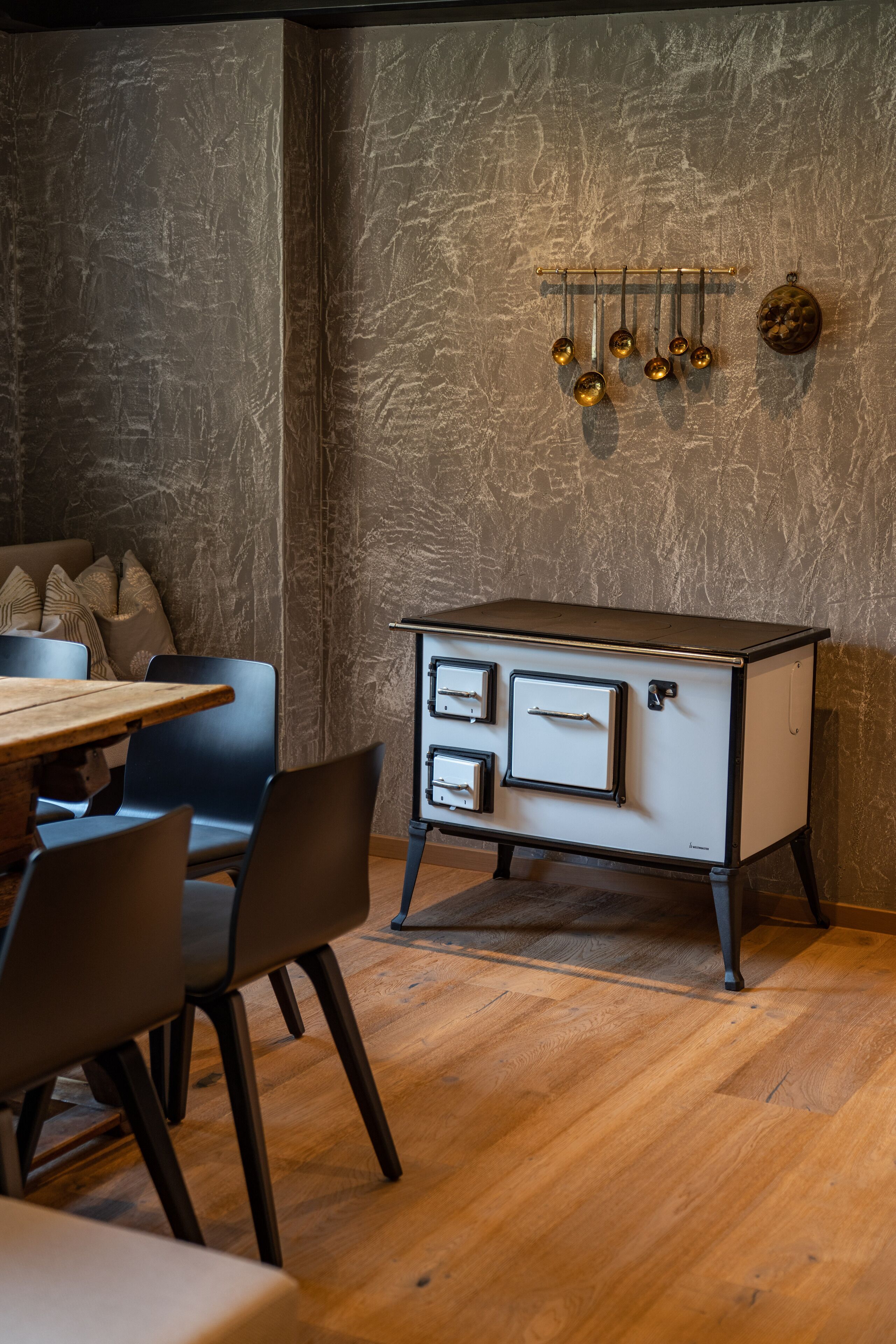 Een eethoek met een houten tafel en stoelen, een kast in vintage-stijl met lades en een gestructureerde wand.