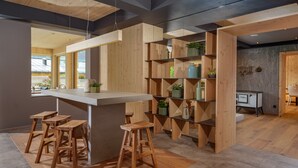 A modern kitchen with a central island, wooden stools, and built-in shelving with plants. - Ferienalm Panorama Hotel & Apartments (Schladming)