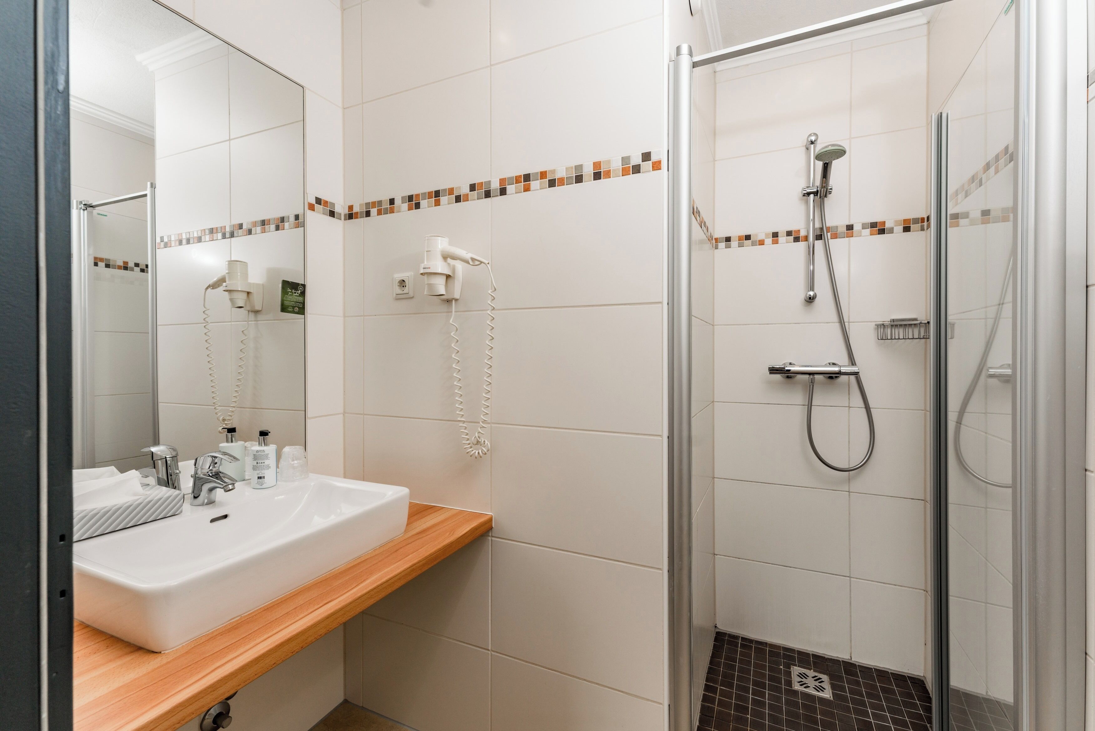 A bathroom with a white sink, a mirror, a shower with a glass door, and a tiled floor.