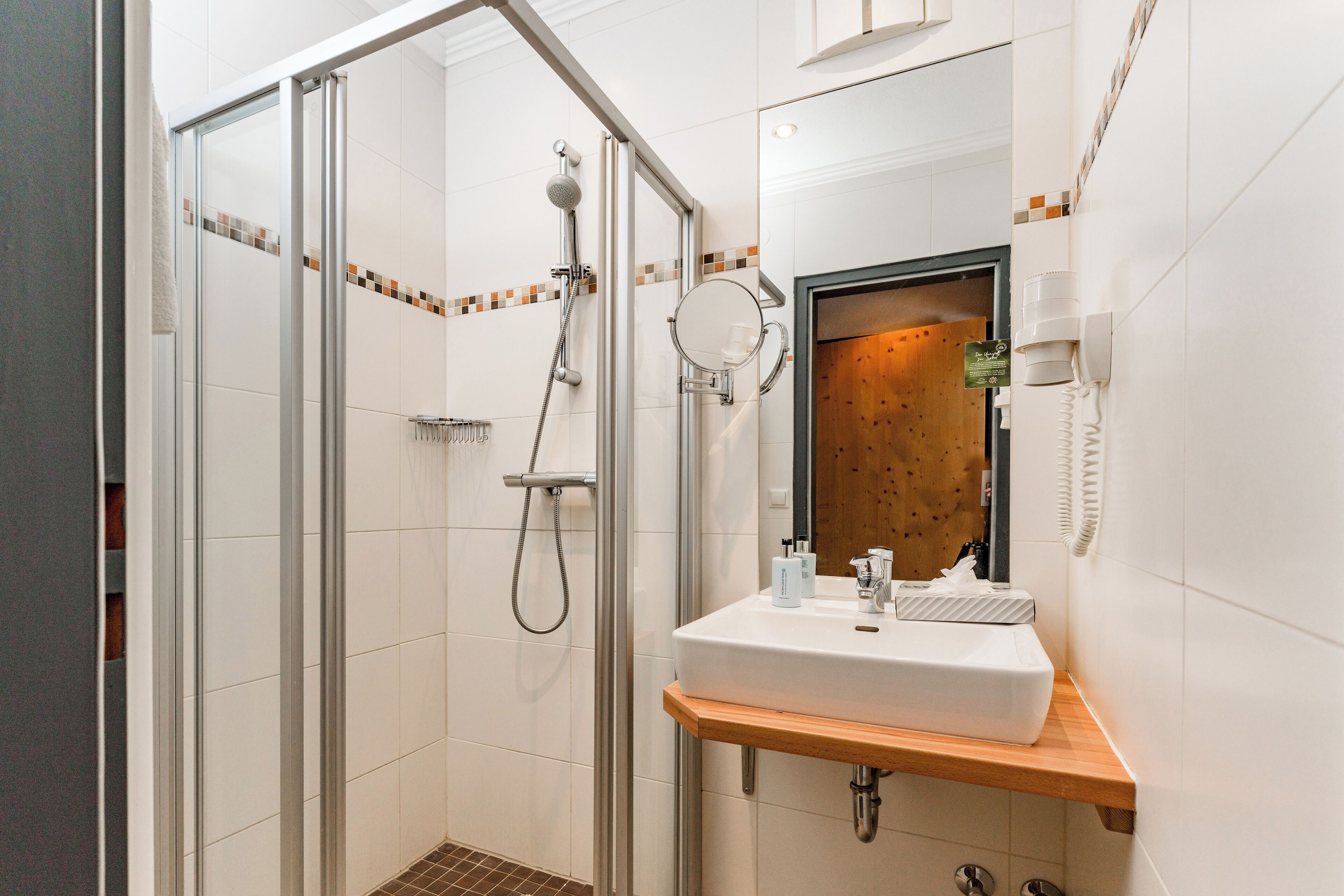 Un baño moderno con ducha envuelta en vidrio, tocador de madera con lavamanos y un espejo.