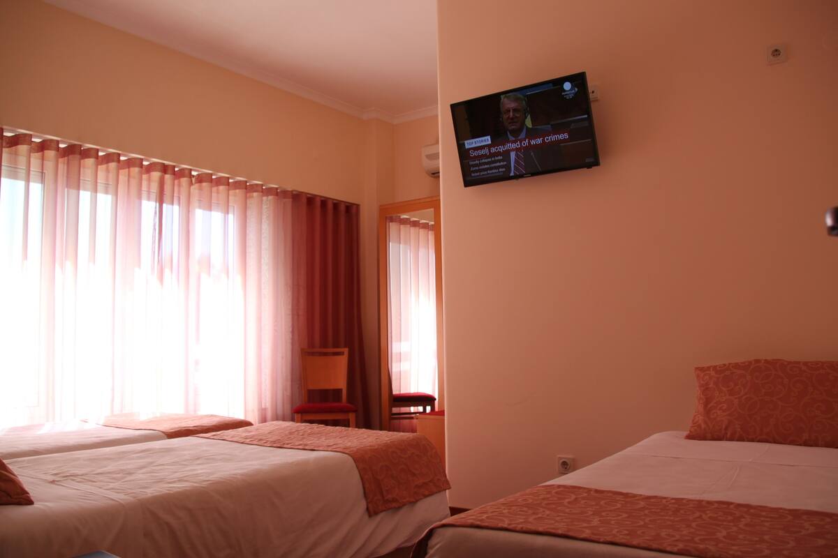 A hotel room with two beds, a TV mounted on the wall, and a window with curtains.