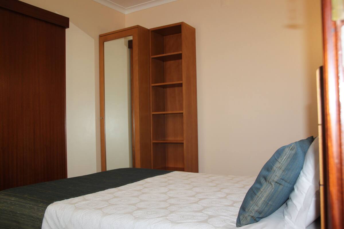 A bedroom with a bed, a wooden wardrobe, and a built-in shelving unit.