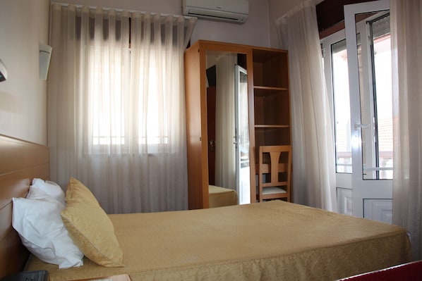 Habitación de hotel con cama, una silla, armario y puerta que da a otra habitación.