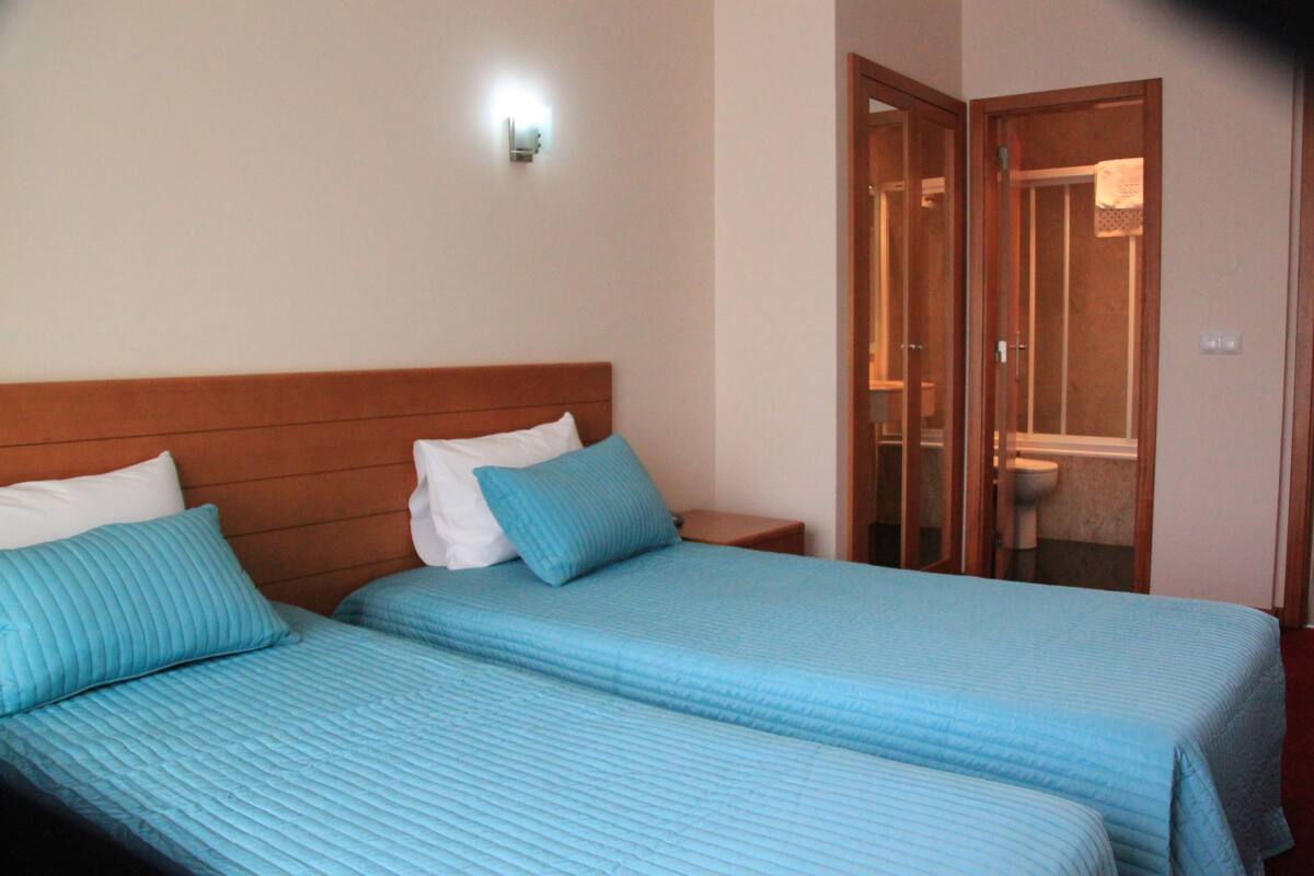 A hotel room with two beds, a wooden headboard, a nightstand, and a bathroom visible through an open door.