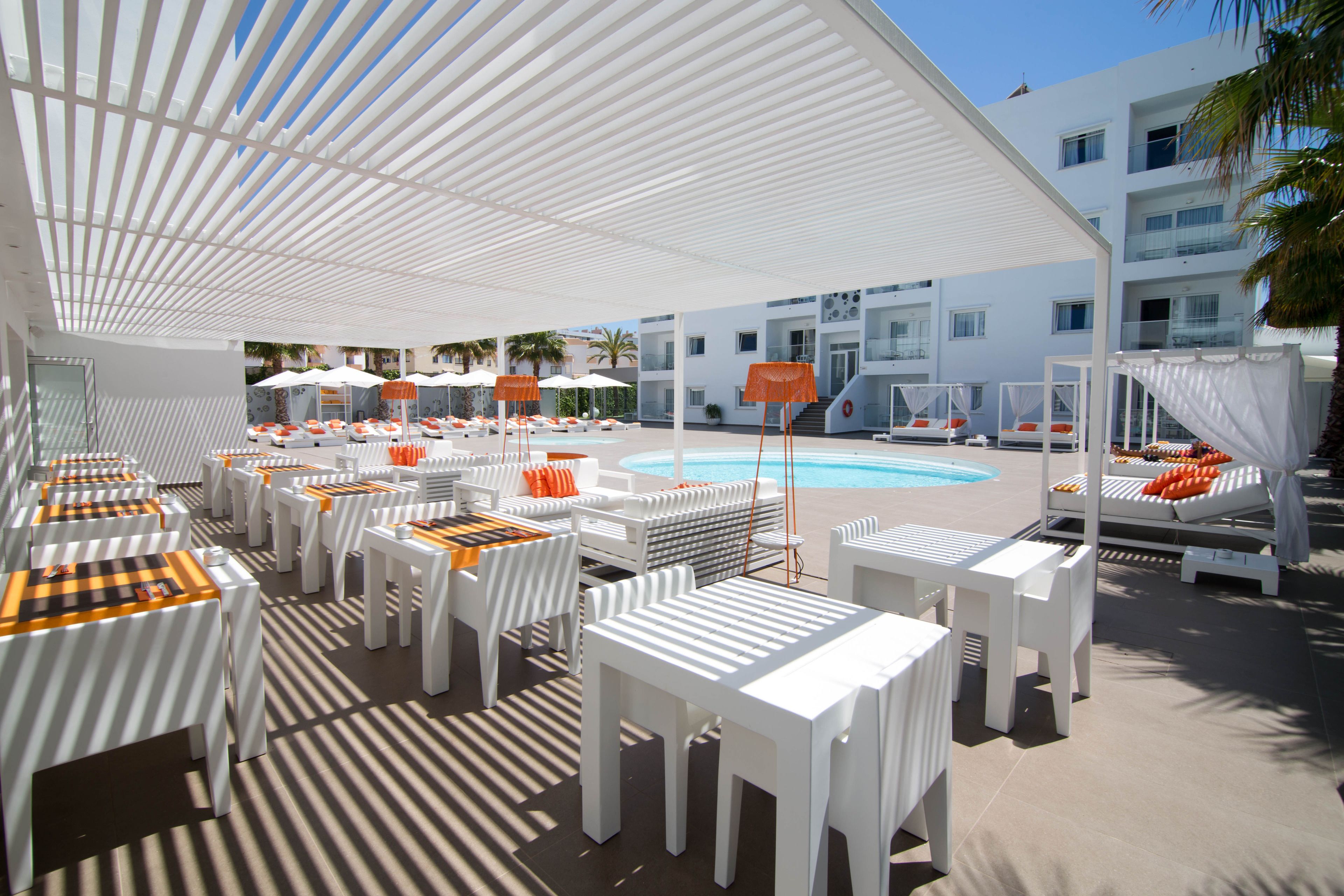 A poolside area with white tables and chairs, umbrellas, and lounge chairs.