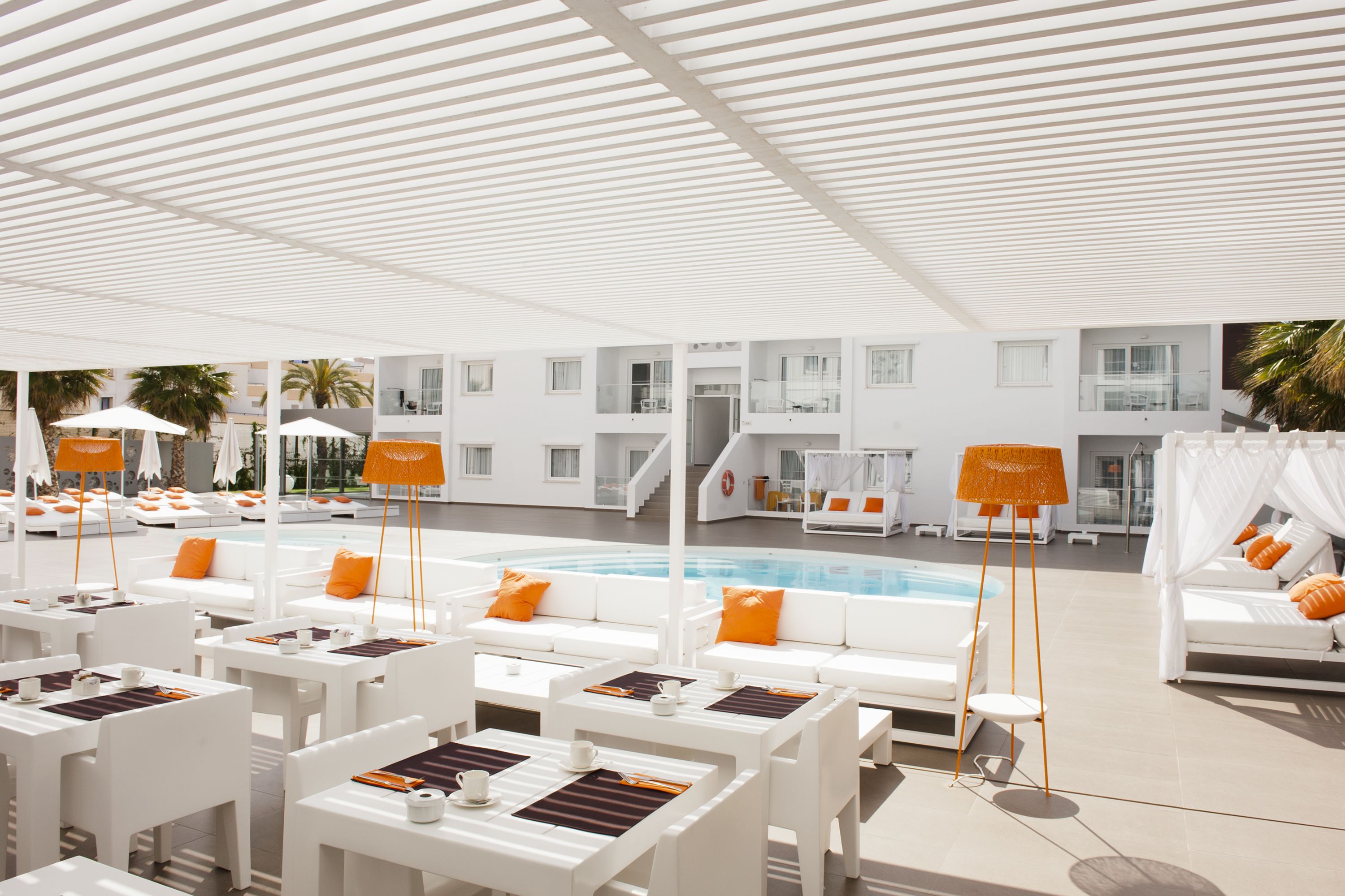 A poolside area with white furniture, orange cushions, and umbrellas.