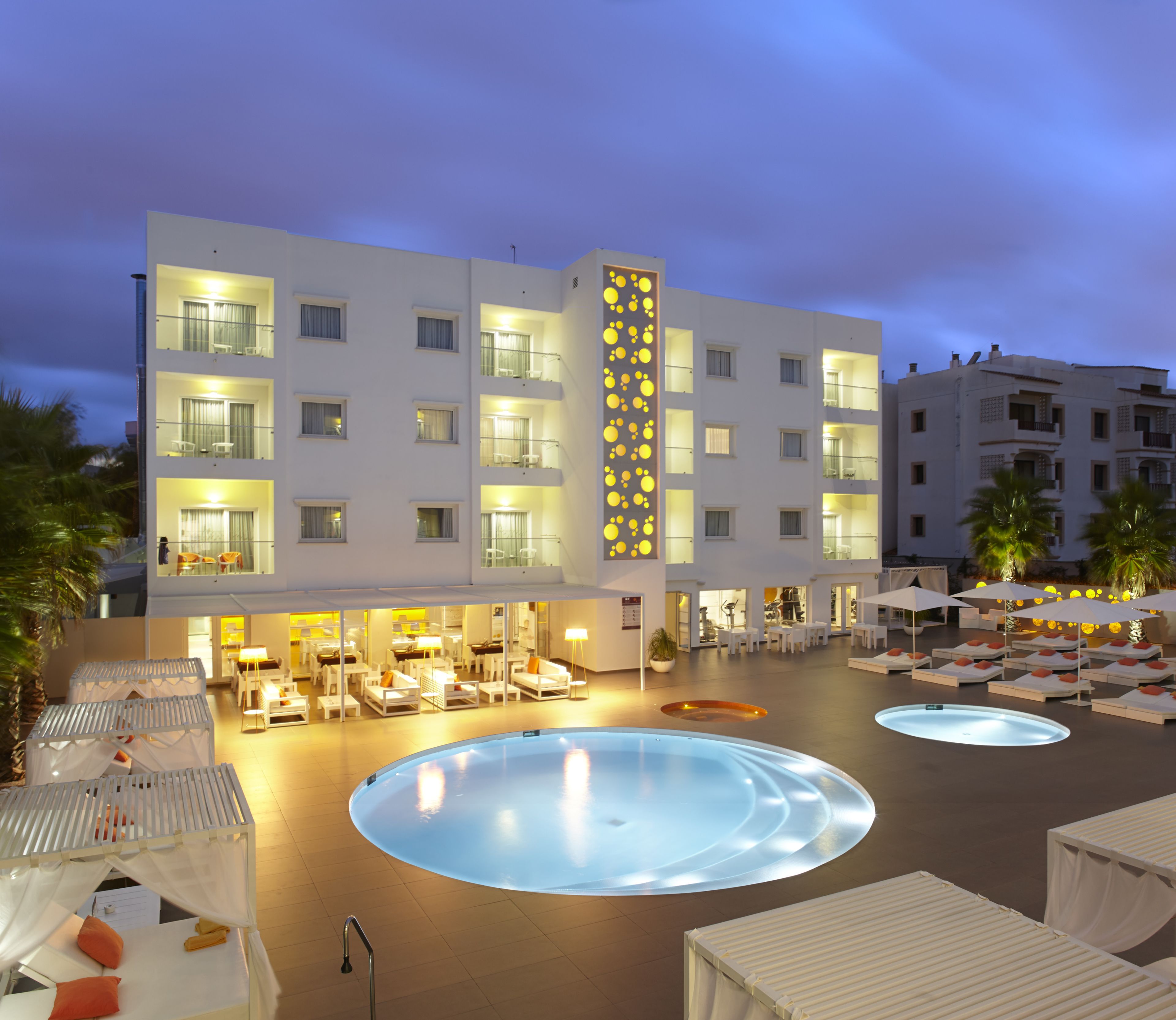 A hotel with multiple balconies, a swimming pool, and outdoor seating areas.