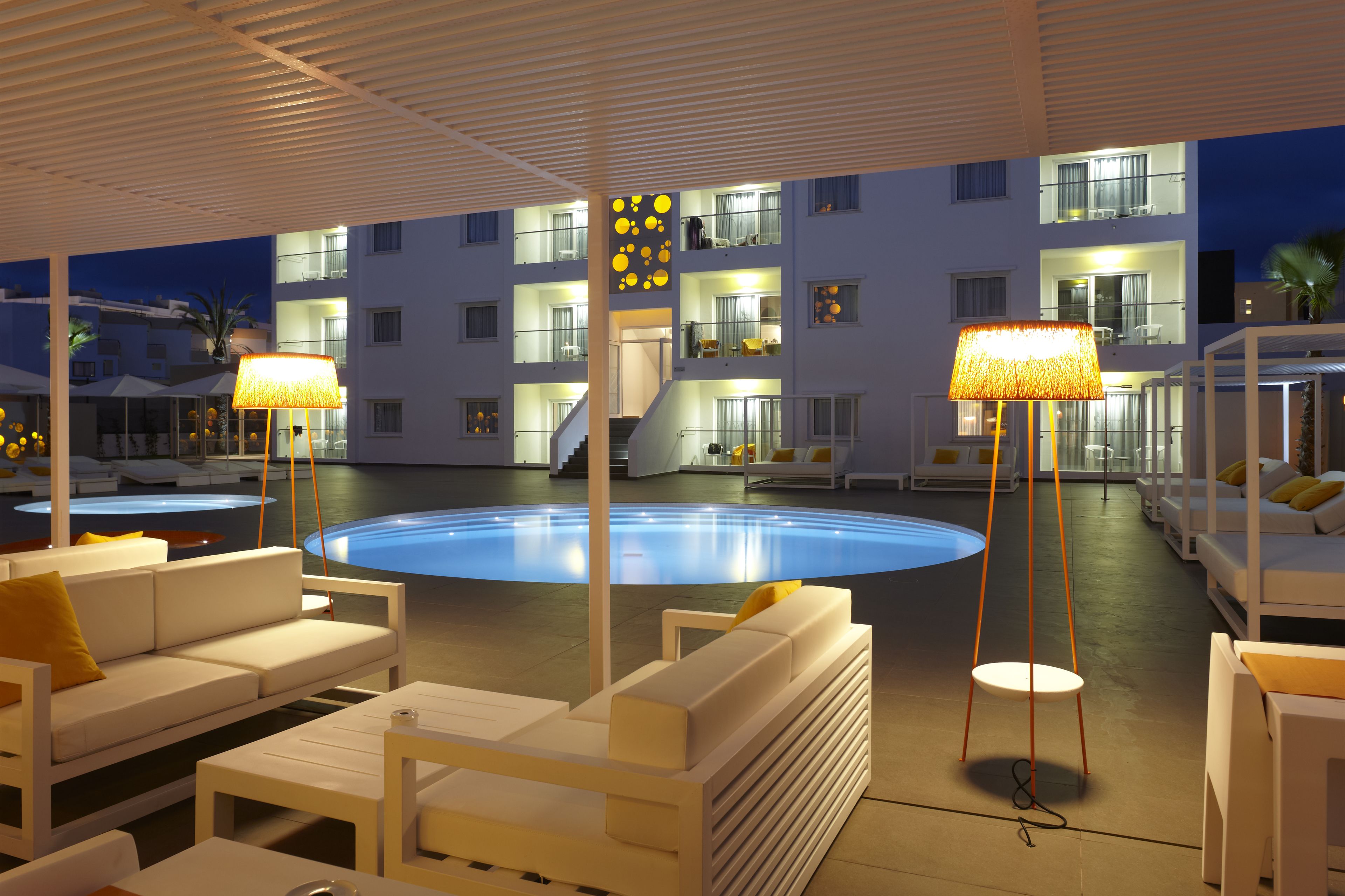 A modern outdoor pool area with white lounge chairs, a circular pool, and two floor lamps.
