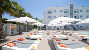 A poolside area with sun loungers and umbrellas, a pool, and a modern building in the background. - Ibiza Sun Apartments (Sant Josep de sa Talaia)