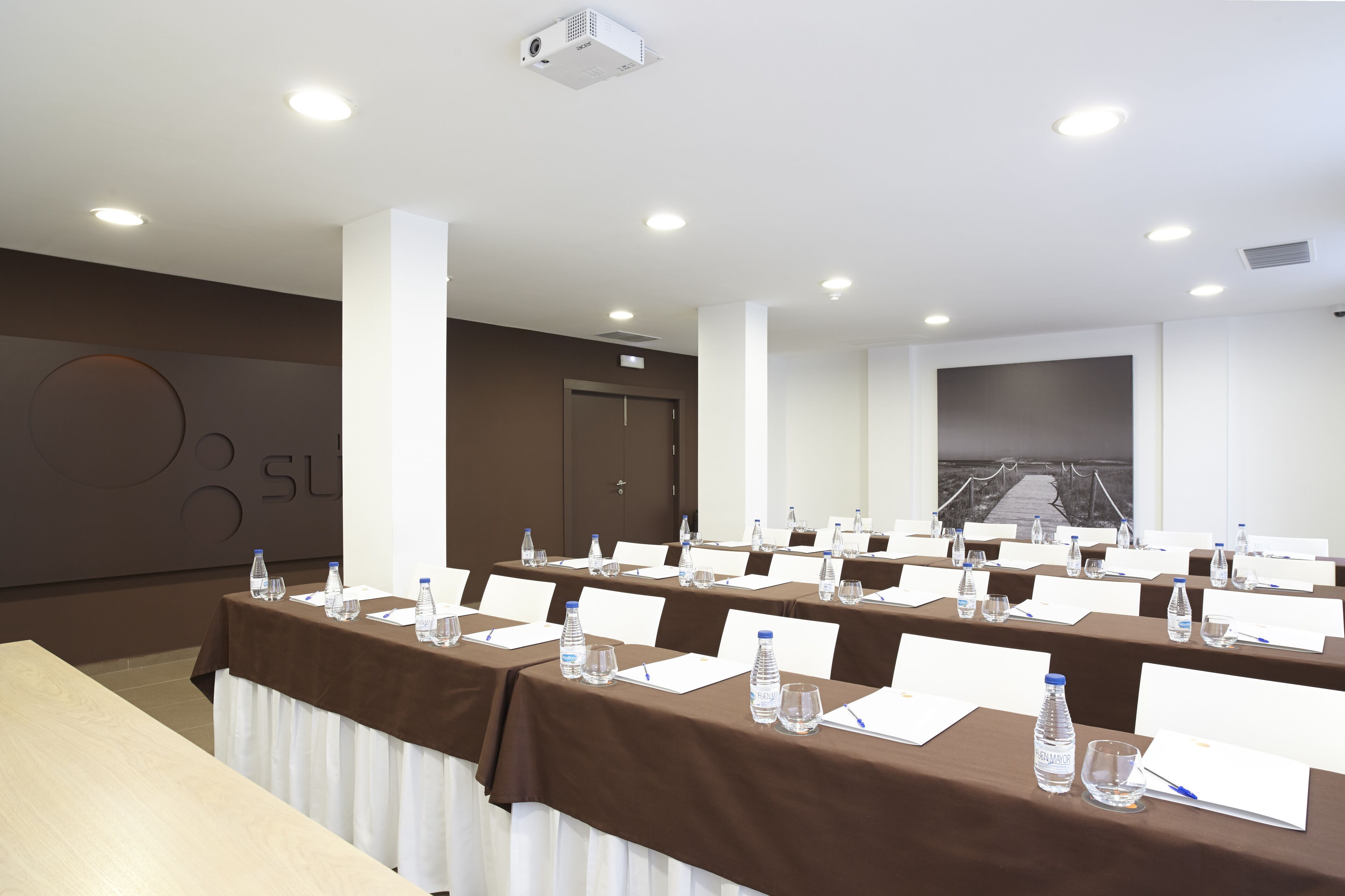 A conference room with long tables, nameplates, water bottles, and a projector.