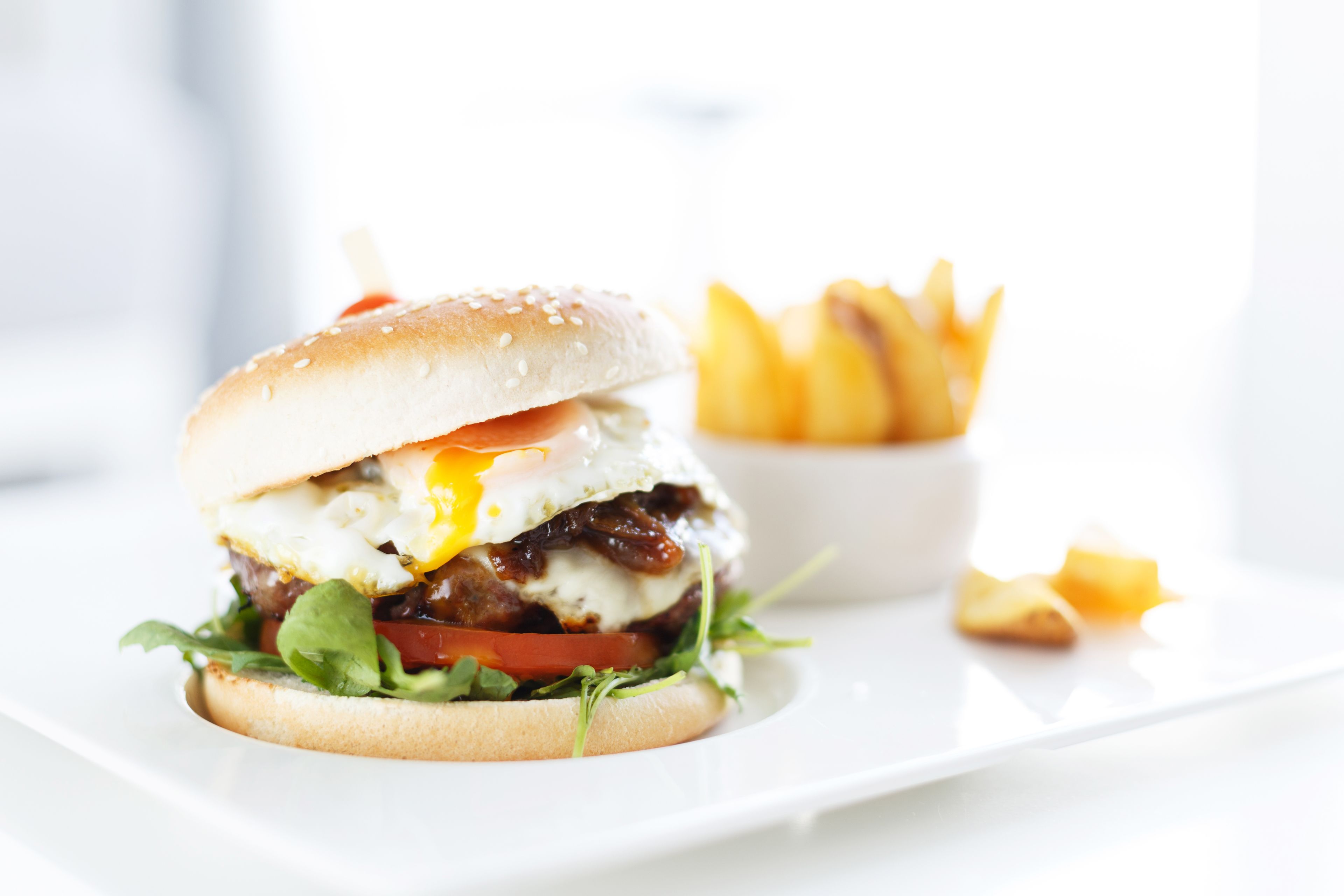 Un hamburger avec un œuf au plat, de la laitue, des tomates et un pain, servi avec une portion de frites.
