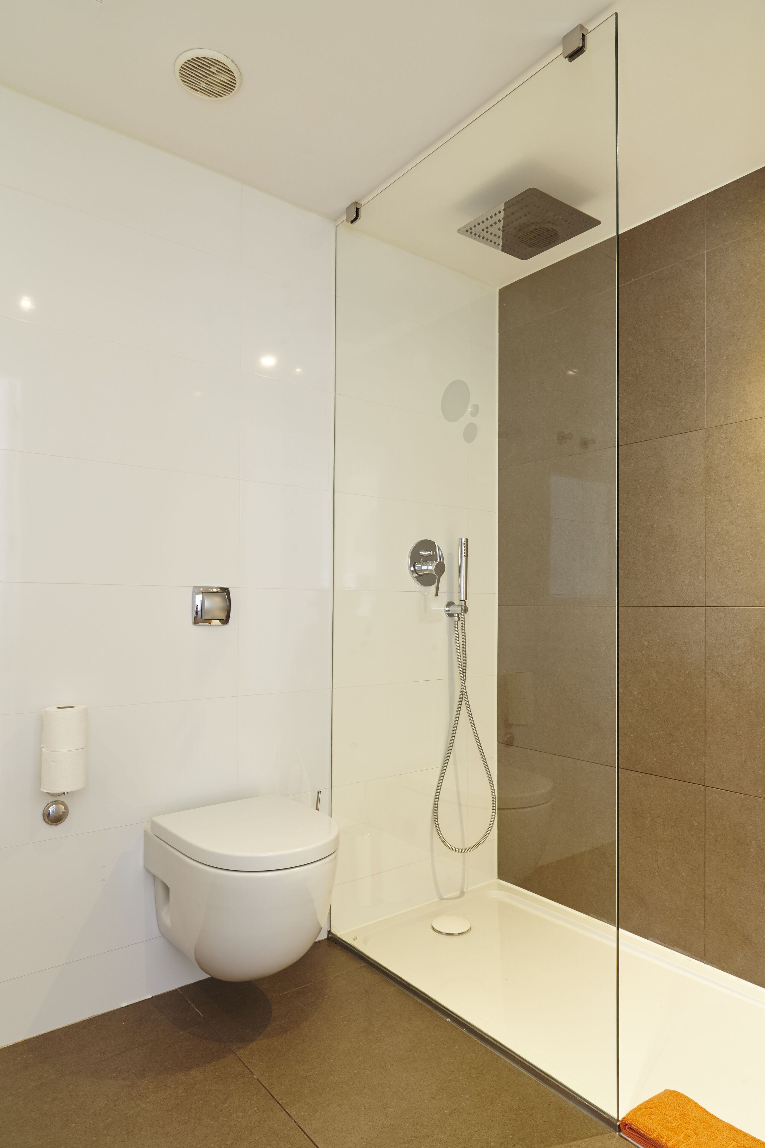 A modern bathroom with a glass shower enclosure, a toilet, and a hand dryer.