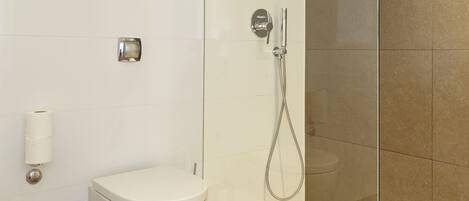 A modern bathroom with a glass shower enclosure, a toilet, and a hand dryer.