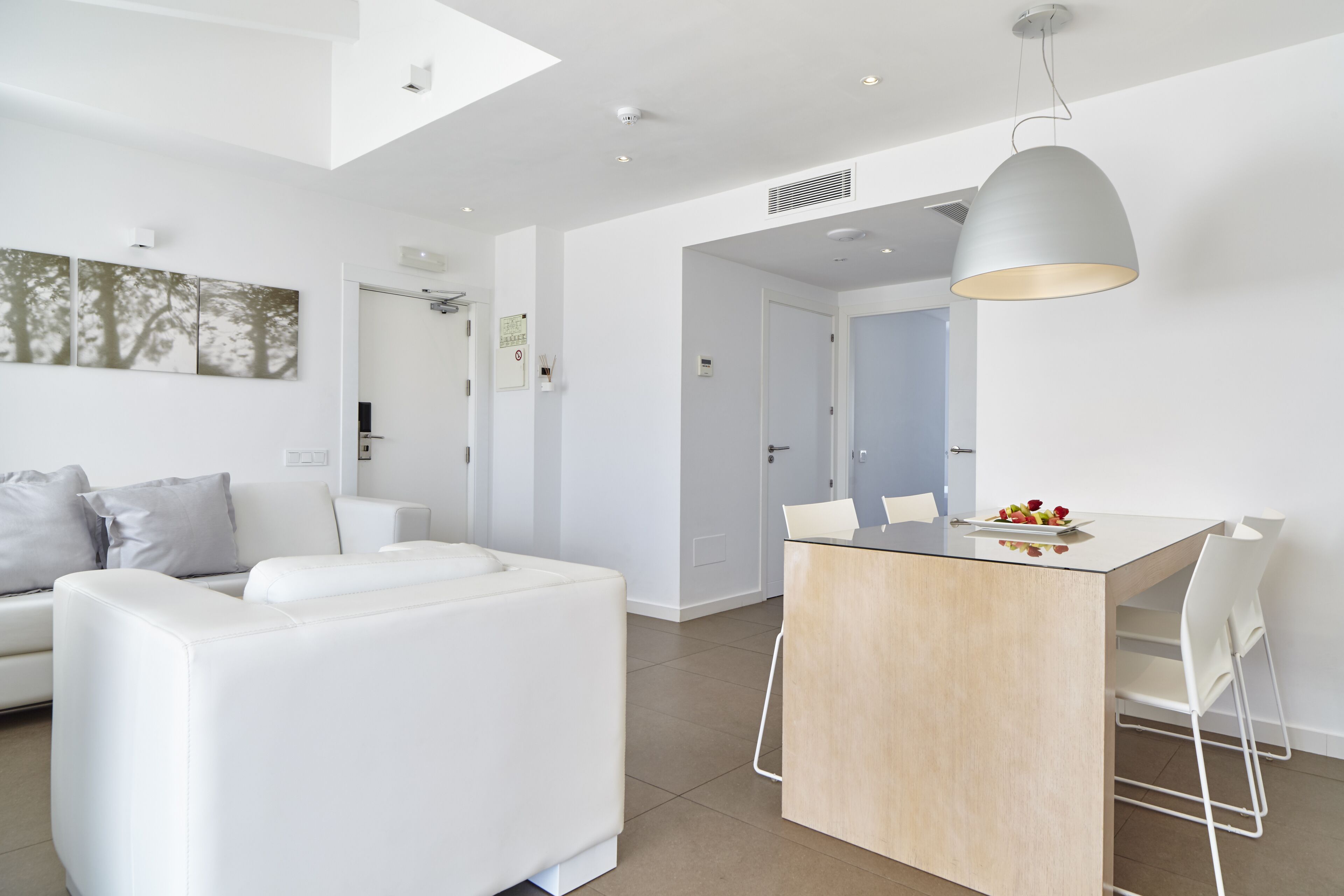 Una sala de estar moderna con un sofá blanco, un comedor con una mesa de vidrio y una lámpara colgante.