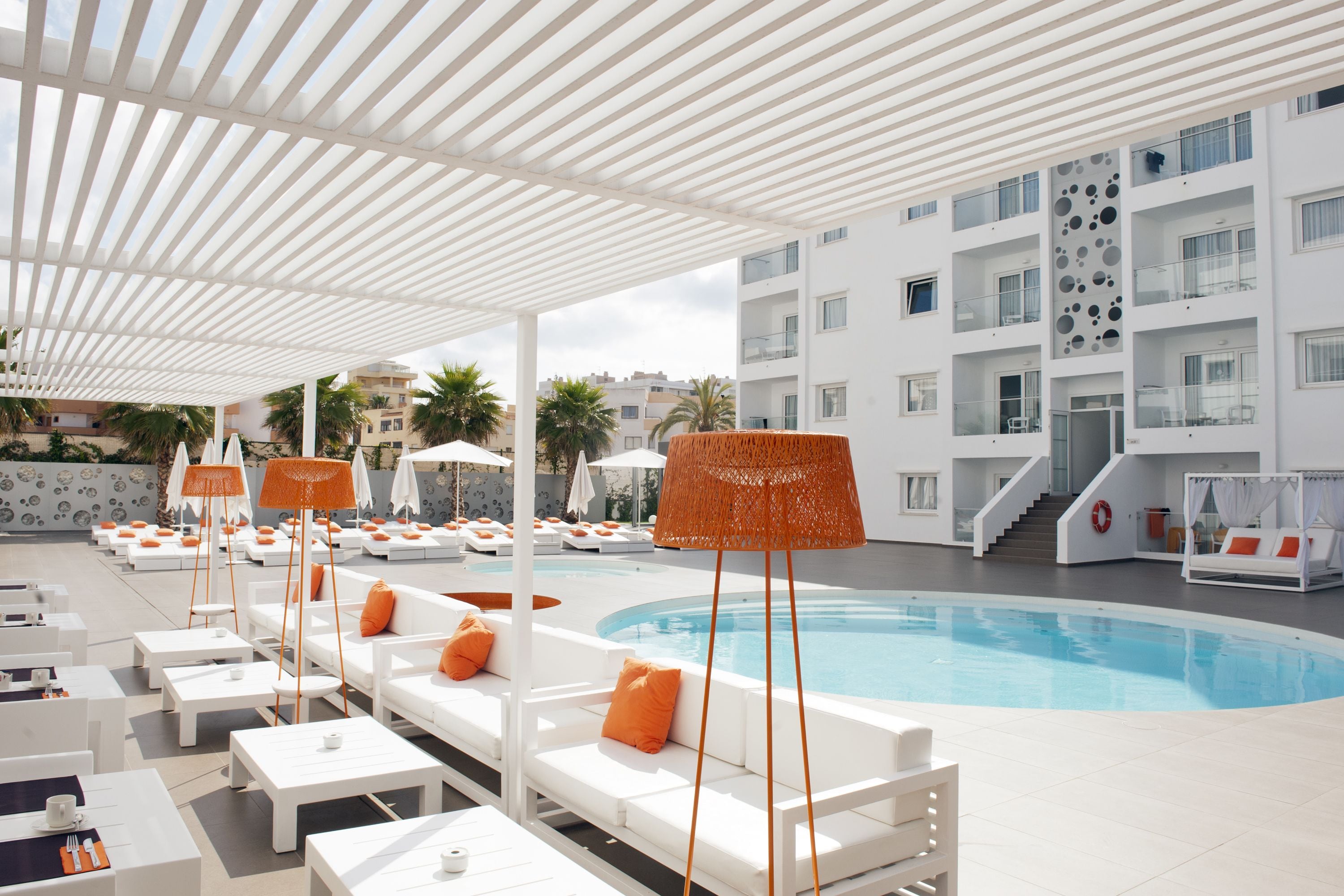 Ein Poolbereich mit weißen Liegestühlen, orangefarbenen Kissen und einem Pool.
