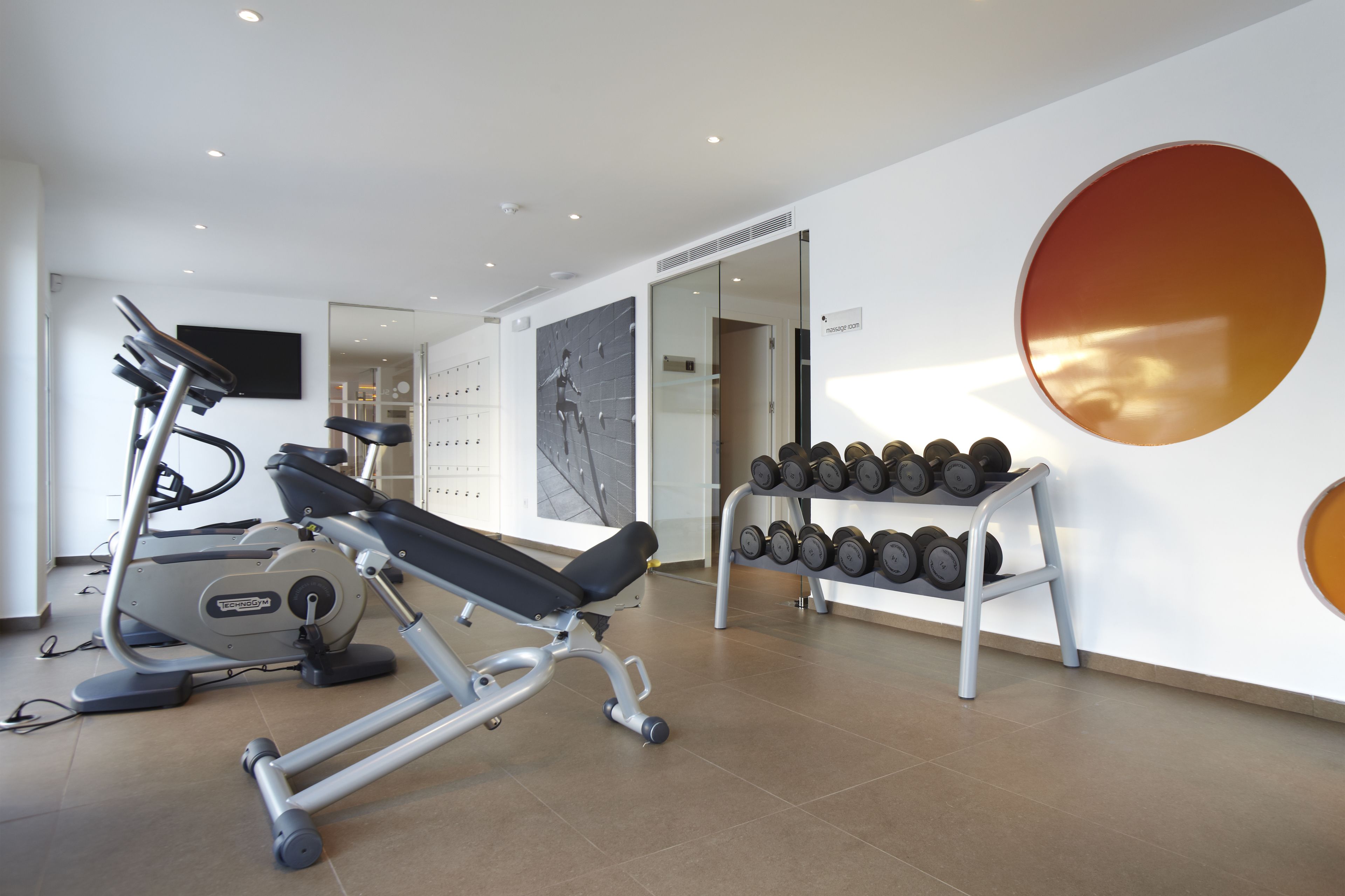 Un gimnasio moderno con equipo de cardio, mancuernas y un espejo grande.