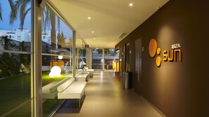 A modern hotel corridor with glass walls, a seating area, and a 'Sun' sign on the wall. - Ibiza Sun Apartments (Sant Josep de sa Talaia)