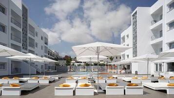 Zona de piscina en la azotea con sillas de descanso blancas y sombrillas, rodeada de edificios modernos.