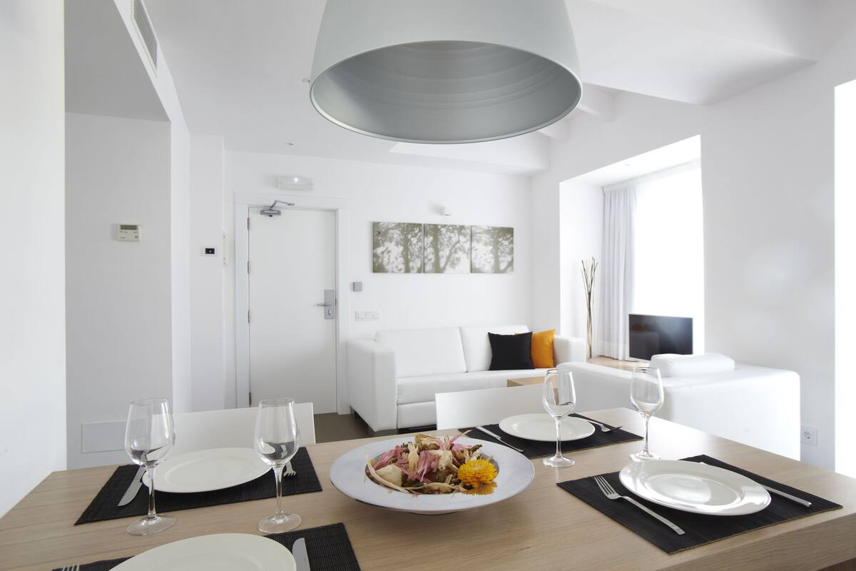 A modern, well-lit dining area with a wooden table set for two, white plates, and wine glasses.