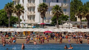 A multi-story hotel with balconies, a beach in the foreground, and palm trees. - Hotel Ca' Bianca (Riccione)