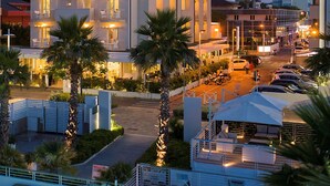 A hotel with multiple balconies, a swimming pool, and palm trees. - Hotel Ca' Bianca (Riccione)