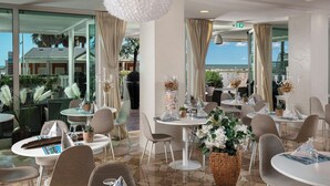 A restaurant with round tables, wicker chairs, and potted plants. - Hotel Ca' Bianca (Riccione)