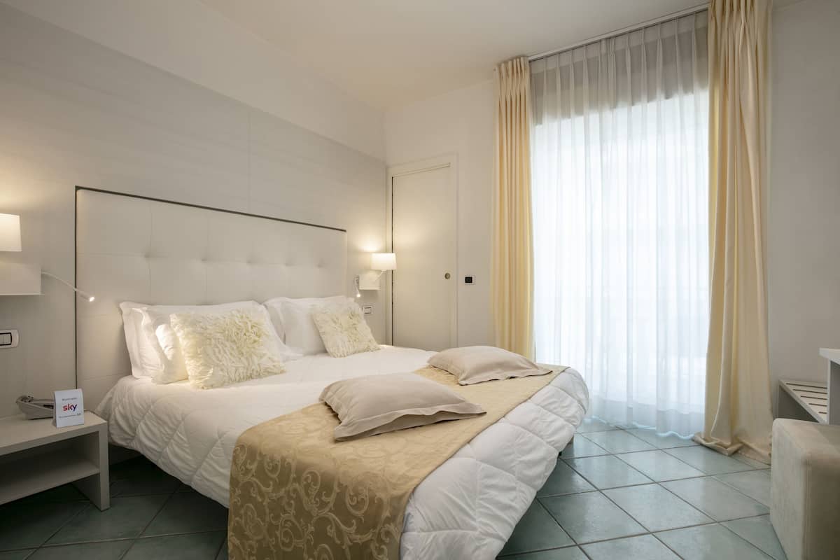 A hotel room with a large bed, bedside tables, a nightstand, and a window with curtains.
