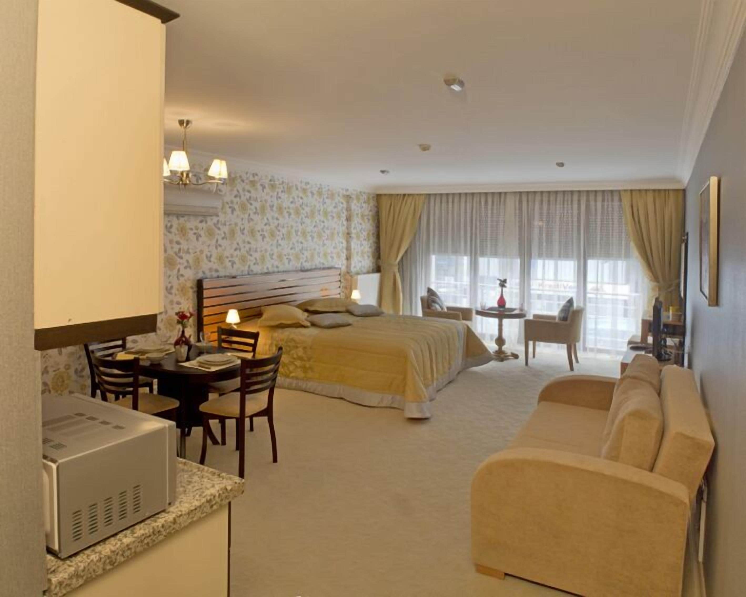 A hotel room with a bed, a desk with a computer, a chair, a sofa, and a small table with a lamp.