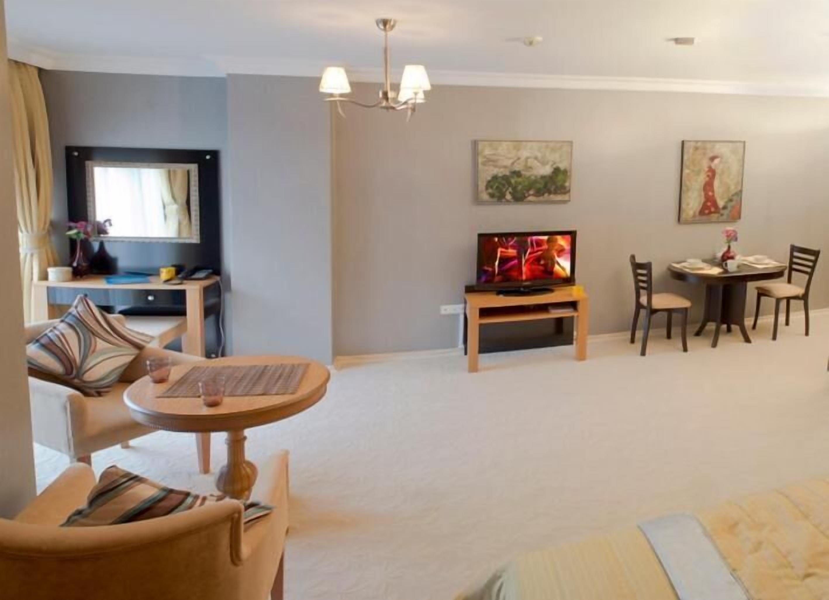A hotel room with a bed, a TV, a dining table with chairs, a small desk, and a sofa.