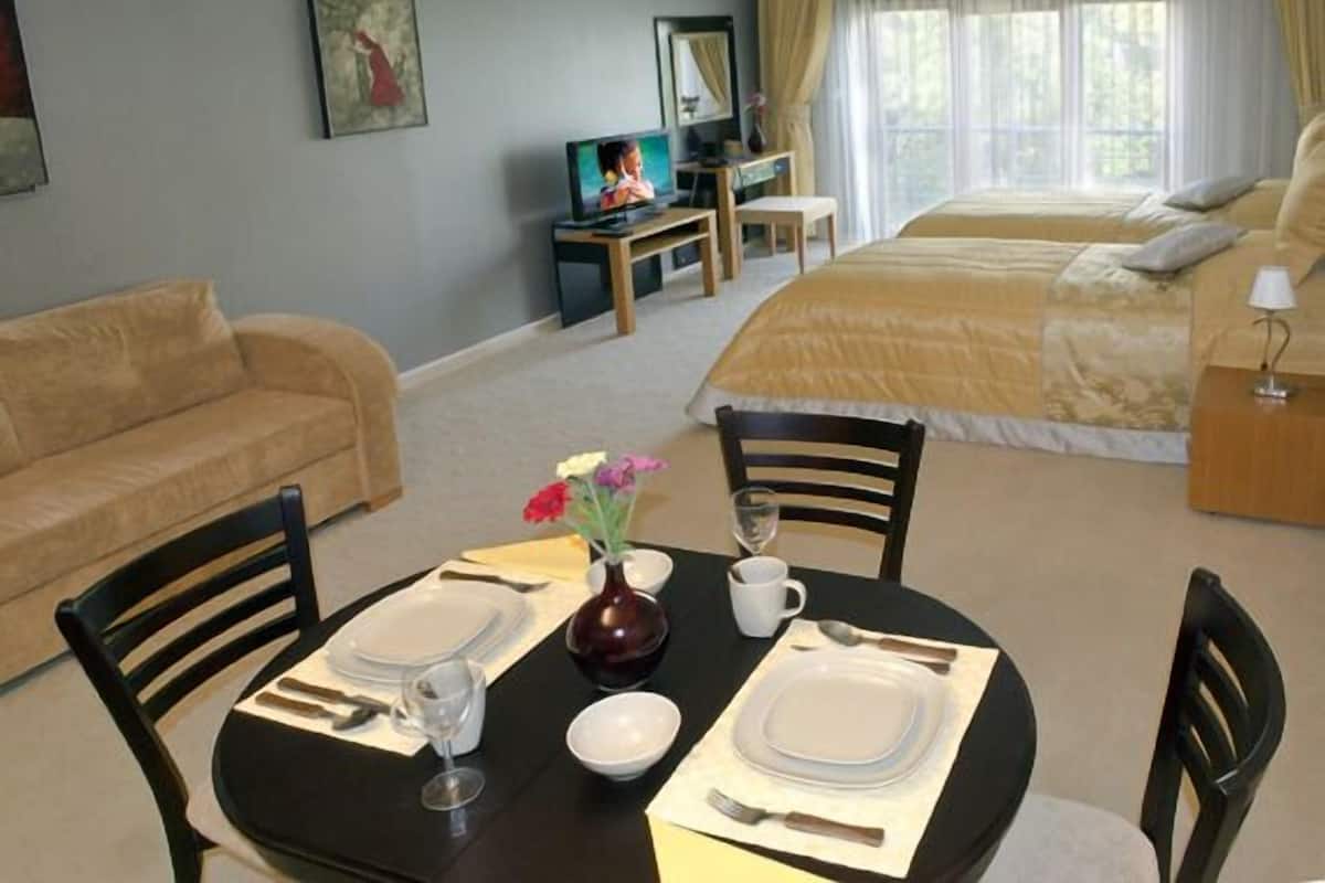 A hotel room with a bed, a sofa, a dining table set for two, a TV, and a window with curtains.