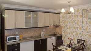 A compact kitchen with a microwave, sink, and dishwasher. There is a dining table with chairs and a vase with flowers. - The Bosphorus Aparts (Istanbul)