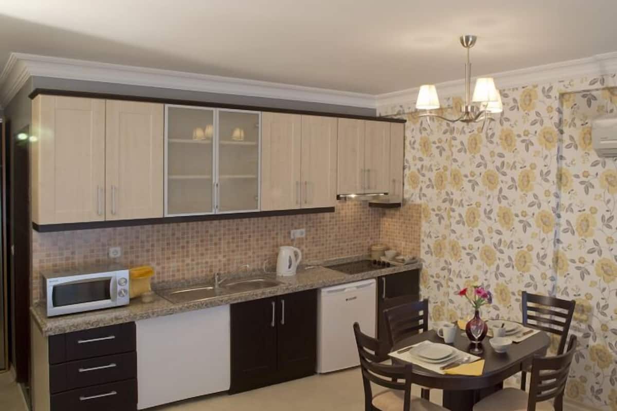 A compact kitchen with a microwave, sink, and dishwasher. There is a dining table with chairs and a vase with flowers.