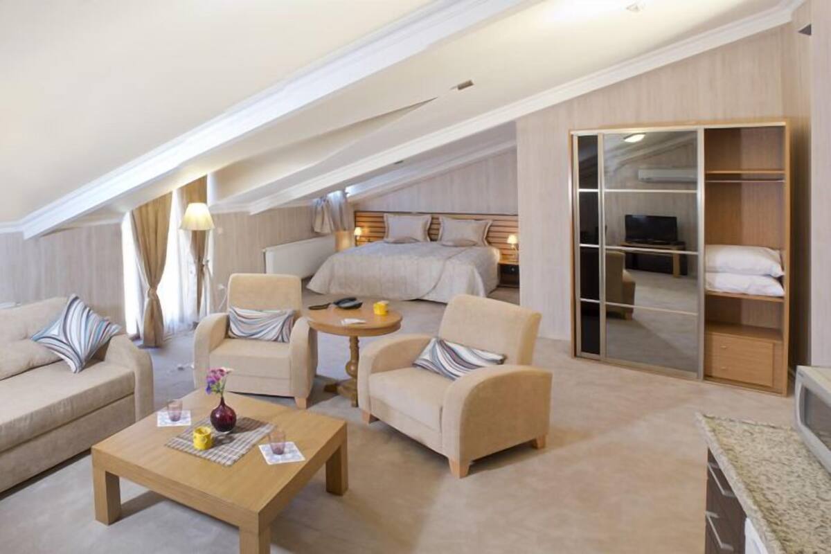 A modern hotel room with a large bed, a seating area with sofas and a coffee table, a walk-in closet, and a television.